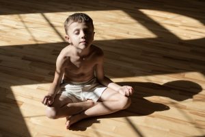 Charming little boy is while doing yoga at home